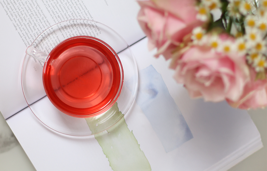 Eine Glasstasse mit rotem Tee auf einem aufgeschlagenen Buch, daneben ein Strauß aus rosa Rosen