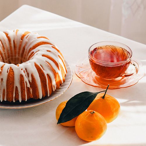 Teetasse auf einem Tisch mit Mandarinen und Kuchen mit weißer Glasur